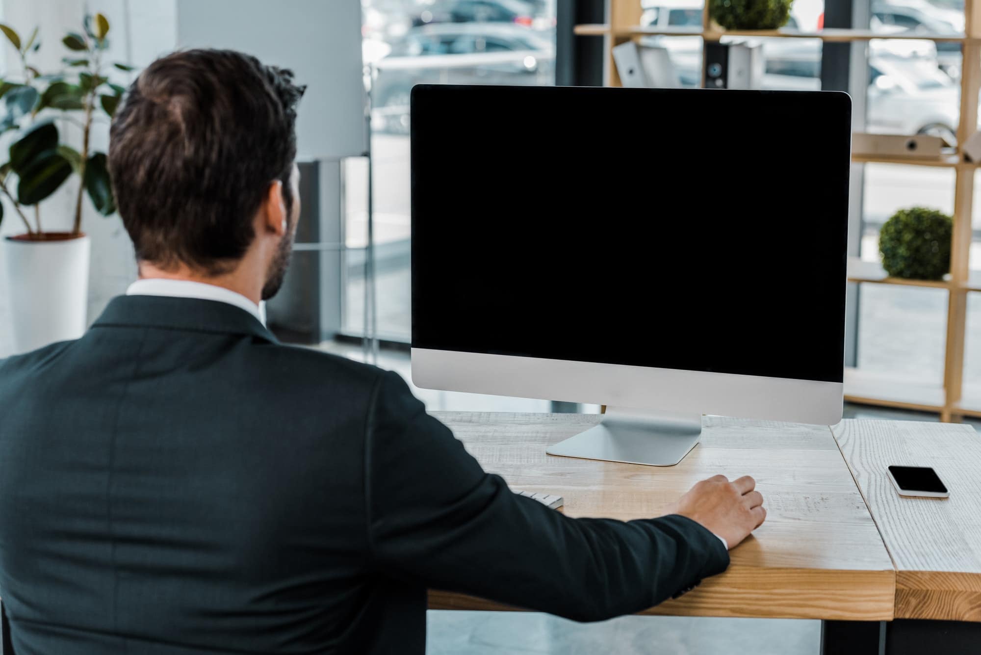 back view of businessman at workplace with computer screen with blank screen in office